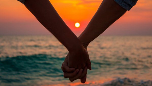 Zwei Personen, welche sich die Hand geben. Im Hintergrund ein Sonnenuntergang