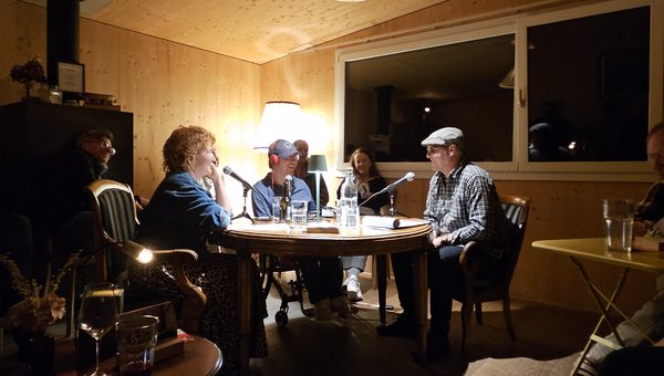 3 Personen an einem Tisch im Gespräch in einer Stube