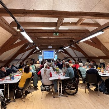 Die Teilnehmenden der GV sitzen an drei langen Tischen und hören zu